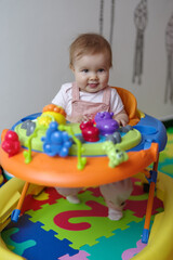 Fototapeta na wymiar Cute baby girl in baby walker at home