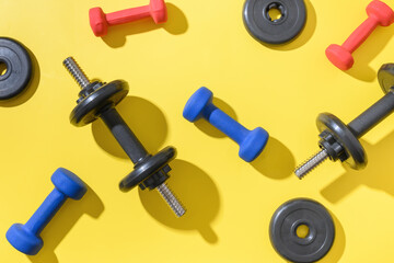 Pattern of colorful dumbbells on yellow background. Sport and fitness. View from above. Flat lay.