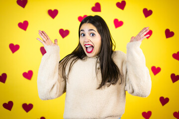 Young caucasian woman over yellow background with red hearts celebrating crazy and amazed for success with arms raised and open eyes screaming excited.winner concept