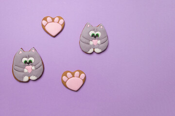 Valentine cookies in form of cats on violet colored paper background with copyspace