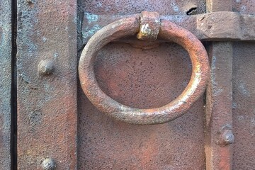 Antique metal door knocker in the form of a ring on a wooden gate close-up. 