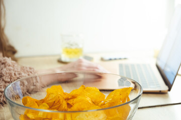 Young woman working at laptop and eating chips