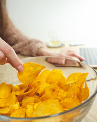 Young woman working at laptop and eating chips