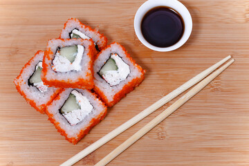 Sushi maki rolls with chopsticks on bamboo table with soy sauce, top view