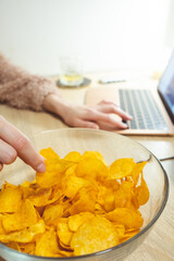 Young woman working at laptop and eating chips