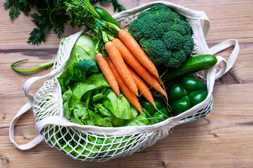 Frisches rohes Gemüse in einer wiederverwendbaren Einkaufstasche auf einem Holz Tisch. Draufsicht,...