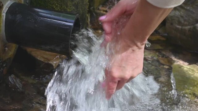 A woman washes her hands in a clean forest spring on a summer day. Water jet close up.