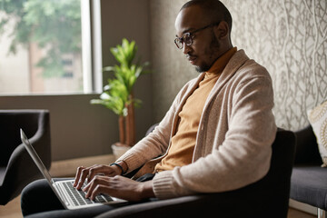 Black african creative writer sitting relaxing and typing on laptop