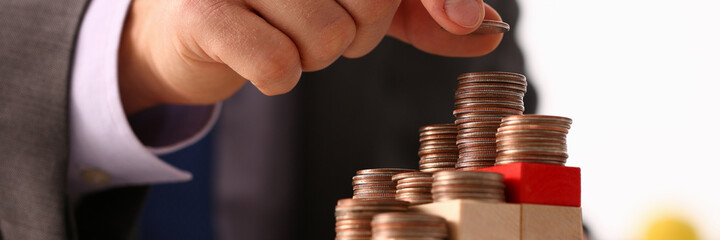 Close up cropped head of man in suit constructing wooden planks and putting coins on top