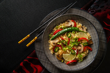 Asian noodles. Noodles with mushrooms and vegetables. Food sticks. Plate with noodles on a dark background.	

