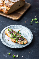 Eine Scheibe Brot mit Butter und frischer Kresse auf einem grauen rustikalen Teller. Schwarzer HIntergrund, gesundes Frühstück, selbstgemacht.