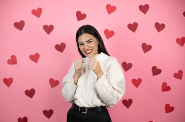 Young beautiful woman over pink background with harts Punching fist to fight, aggressive and angry attack, threat and violence