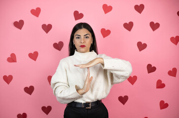 Young beautiful woman over pink background with harts Doing time out gesture with hands, frustrated and serious face