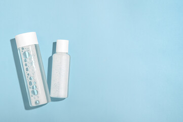 Moisturizing lotion, micellar water in white plastic bottles on a blue background top view. Cleansing and refreshing natural makeup remover. Shampoo in a transparent package. Copy space, flat lay