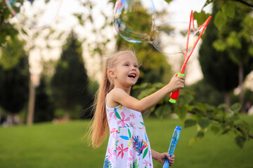 Happy little girl playing with summer soap bubbles in the park.