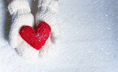 Female hands in knitted mittens with red heart against snow background