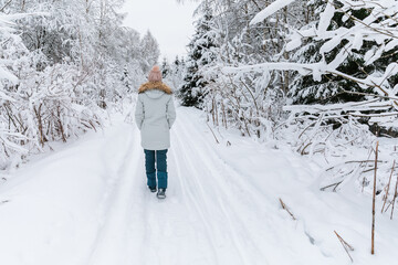 Young woman walking on snow covered forest. Beautiful winter time. Back view.