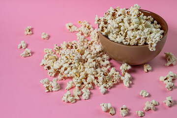 Popcorn on a pink background. A full plate of popcorn. Popcorn is scattered around. Movie snack
