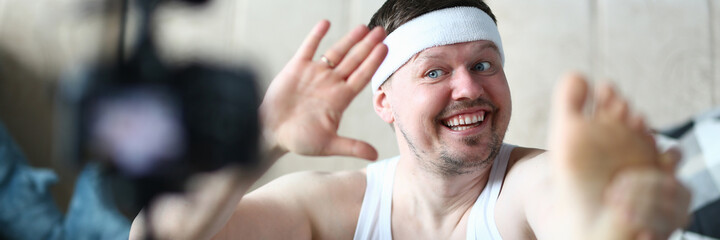 Obraz premium Cheerful overweight man keeping smile on his face while waving hand on camera, stretching his leg