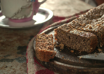budín integral y artesanal sobre un plato de madera, tocado por un haz de luz que entra por la ventana y con tazas de te alrededor