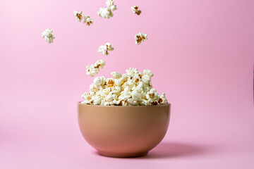 Popcorn on a pink background. A full plate of popcorn. Popcorn falls down. Movie snack.