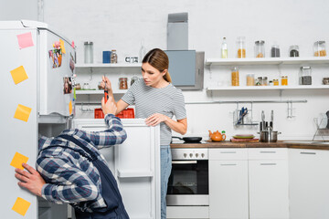young woman giving screwdriver to handyman repairing fridge in kitchen