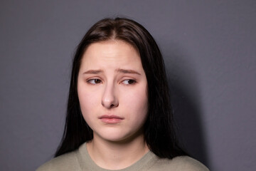 portrait of charming sad brunette woman in marsh color t-shirt on grey wall background. actress acting, emotion