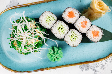 maki rolls with salmon and cucumber in a serving with chuka salad and peanut sauce on a blue plate close-up. vegetarian dish. healthy food concept.. © Pavel