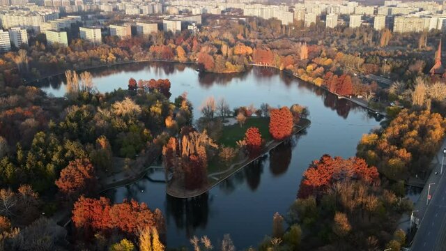 View of the Titan park from the drone with multiple yellowed and red trees, reflecting sky, residential buildings, Bucharest, Romania
