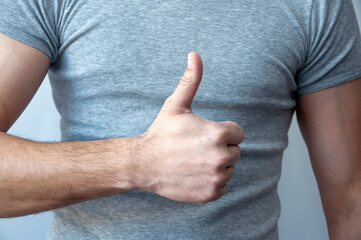 Happy young caucasian man in a gray t-shirt makes a thumb up sign showing his support, respect  and...