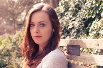 Naklejka premium Portrait of young woman sitting on park bench in soft sunlight