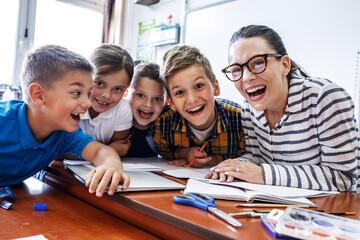 Portrait of a kind female teacher surrounded by her elementary school students, making learning...