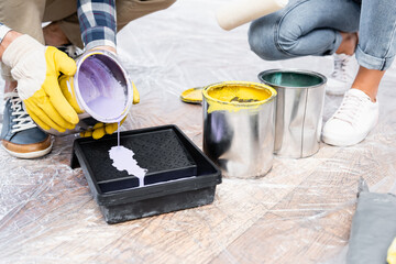 cropped view of young man in gloves pouring paint in roller tray on floor indoors