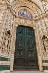 Fototapeta na wymiar Great close-up view of Florence Cathedral's huge bronze doors of the central portal and a lunette above with a colourful mosaic of Christ enthroned with Mary and John the Baptist designed by Barabino.