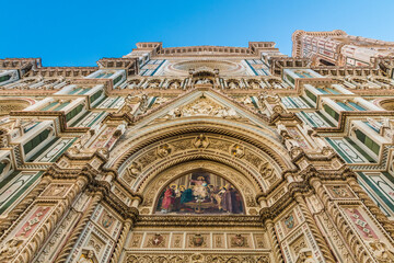 Impressive low-angle view of Florence Cathedral's main facade; from the lunette of the central portal with a colourful mosaic of Christ enthroned, up to the pediment, the rose window and the tympanum.