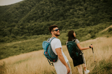 Smiling couple walking with backpacks over green hills