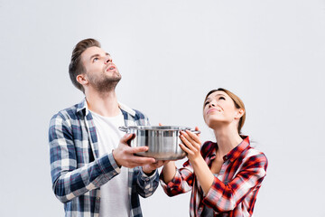 young couple looking up while holding pot under leaking ceiling