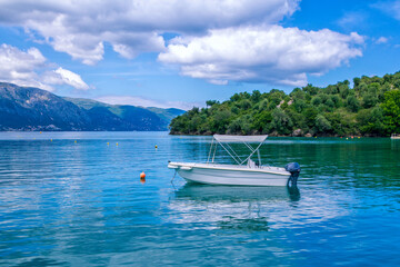 Sea lagoon with calm clear blue water, small white cruise boat, clouds on the sky and mountains on the horizon – summer landscape