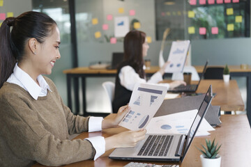 Businesswoman typing on laptop holding papers preparing report analyzing work results in office.