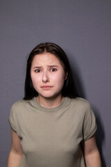 portrait of charming scared brunette woman in marsh color t-shirt on grey wall background. actress acting, emotion