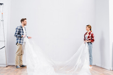 full length of happy young couple with polyethylene covering room at home