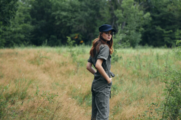 Fototapeta premium Woman in the woods in a gray jumpsuit blue cap back view 