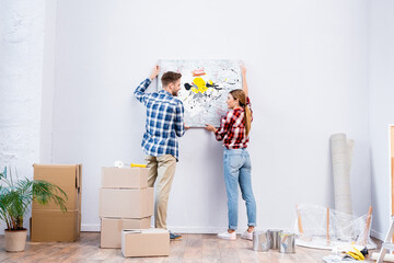 full length of smiling young couple looking at each other while removing picture at home