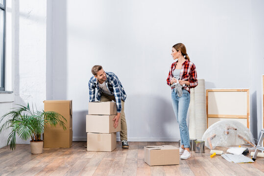 full length of smiling man with cardboard boxes looking at woman holding gloves at home