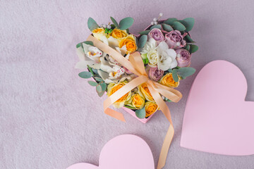 Flowers bouquet arrangement in heart pink hatbox. White orchid, purple and yellow roses with bunch for present to valentine day. Gray background copy space. Mothers day concept.