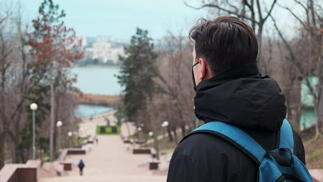 A man in black medical mask and a winter jacket with blue backpack, park on the background in Chisinau, Moldova