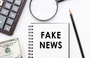 Notepad with FAKE NEWS note on desk with calculator, dollars and magnifier.