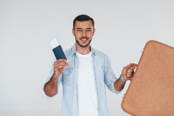 Tourist with ticket. Young handsome man standing indoors against white background
