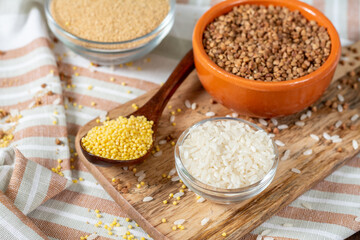 Rice, buckwheat, amaranth and millet in bowls on a brown wooden table. Gluten-free cereals