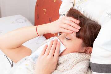 a young pretty girl is sick at home in bed and blows her nose in a handkerchief